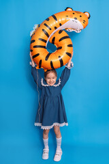 Birthday girl in a dress with a cap on her head holding a balloon in the shape of a six and a tiger...