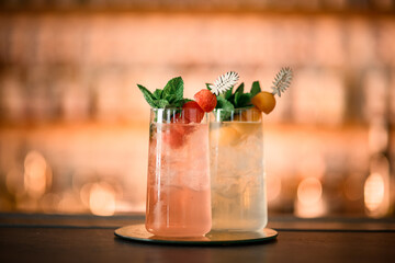 Two tall glasses with iced cocktails, decorated with fruits and green mint leaves