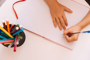 The girl writes with a pen with her left hand in a notepad on a white table.
