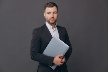 Portrait of successful and confident businessman in grey suit, working with laptop and smiling...