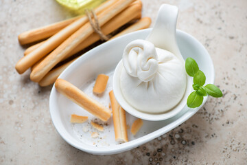 Burrata cheese and grissini or italian bread sticks, horizontal shot on a beige granite background, selective focus