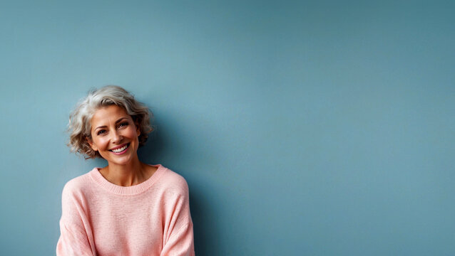 smiling  woman in menopause age in pink sweater over a light blue background with copy space 