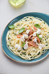 Plate of lemony spaghetti with smoked salmon and feta cheese, vertical shot on a light-beige granite background