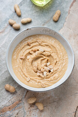 Bowl of freshly made peanut butter on a grey and roseate granite background, vertical shot, elevated view