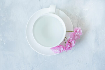 white porcelain cup and saucer with water and pink sakura flowers on a light gray background with a putty effect. Minimalism of details. pale tone. Flat top view