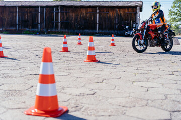 L-driver person drives slalom through the orange cones on motordrome on motorcycle