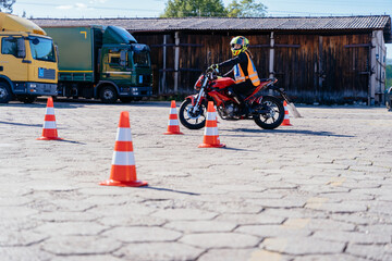 L-driver person drives slalom through the orange cones on motordrome on motorcycle