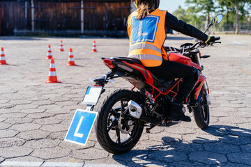 L-driver person drives slalom through the orange cones on motordrome on motorcycle