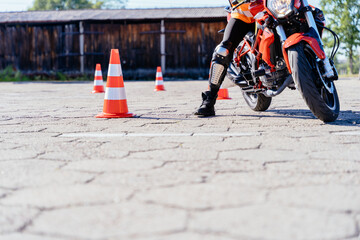 L-driver person drives slalom through the orange cones on motordrome on motorcycle