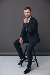 Stylish business man,  male sitting on a designer chair. Portrait of the beautiful posing in a Studio. Gray background, isolated.