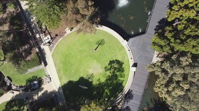 Aerial ascending view over circular grass area of landscaped park with fountains