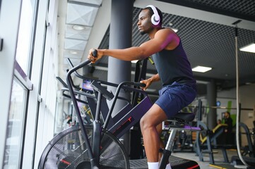 Athletic black man doing cardio workout on exercise bike in gym. Concept of sport and healthy...