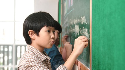 Side view of asian boy writing engineering prompt and programing system while standing blackboard...