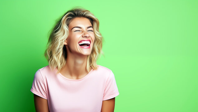 Belle femme aux cheveux blonds, &acirc;g&eacute;e de 25 ans, heureuse et riant aux &eacute;clats sur un fond vert, portant un t-shirt rose, image avec espace pour texte.