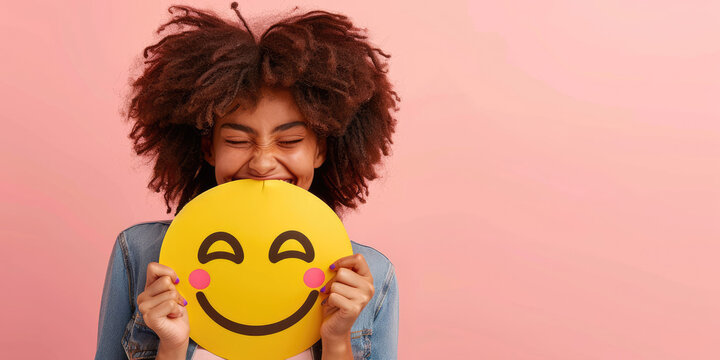 woman holding up an emoji face on pink background, smiley happy person smiling and showing emoticon symbol with eyes closed