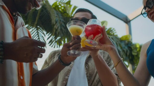 Low angle of biracial friends in glasses toasting with cocktails when visiting trendy cafe