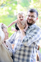 Parents joyfully hold smiling baby girl outdoors, capturing a h