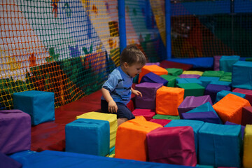 Сhild plays in an entertainment center among colored foam cubes.