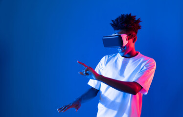 Young African American gaming player wearing VR pointing hologram 3D graphic isolated blue pink...