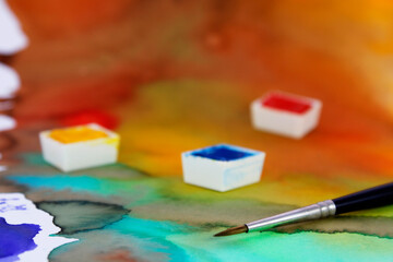 Solid watercolor tablets and brush on abstract background