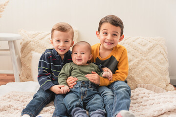 Toddler brothers sitting together on blankets & pillows and smiling
