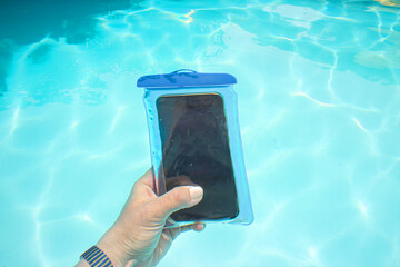 Hand holding smartphone in bag in beautiful blue pool, tropical location. Concept of influencer...