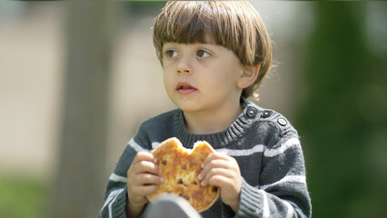 Young Child Eating Freshly Baked Pizza Outside on a Sunny Day, Dressed in a Striped Sweater, Focused and Enjoying His Meal