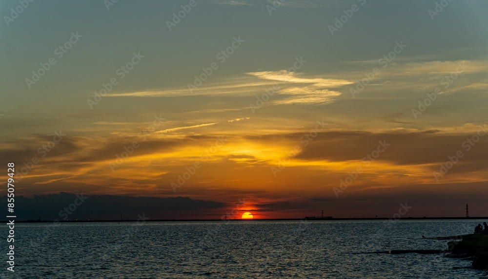 Canvas Prints Sunset over a calm sea with a vibrant sky and silhouettes on the shore