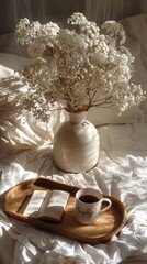 a flowers bouquet in a vase on a wooden tray, accompanied by a book and coffee cup, set against a serene white bed background.