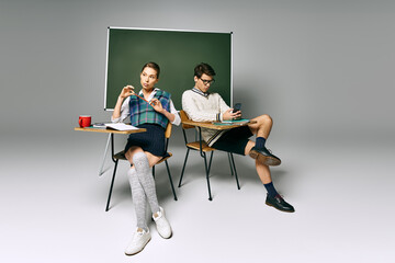 Fototapeta premium Two young students sitting at a desk in front of a green board in a college classroom.
