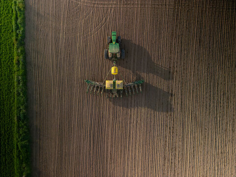 Ontario Canada May 13 2022: Aerial view of a large modern John Deere tractor plowing farmland field in spring season. Drone photo. Farming, agriculture concept.