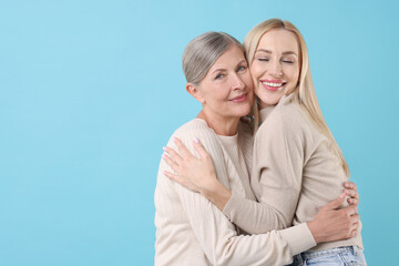 Fototapeta premium Family portrait of young woman and her mother on light blue background. Space for text