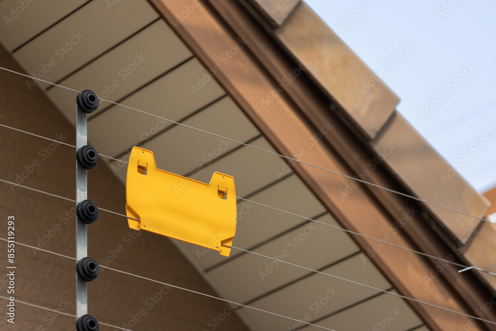 Wall mural a yellow sign is attached to a fence. security electric fence with yellow tag.