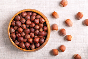 Hazelnuts in a wooden bowl on linen fabric. Whole, dried and shelled nuts of Corylus avellana. Ready to eat as snack, and also used for baking. Nuts in their shells on the right. Close-up, from above.