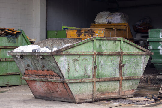 A green dumpster with a red lid sits in a lot