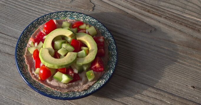 Pico de Gallo salsa and avocado slices on a red corn tortilla. Rustic wooden background with copy space. Table spin.