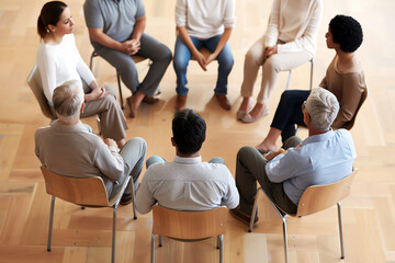 A group of diverse people sit in a circle and talk. They are all wearing casual clothes and look like they are in a support group.