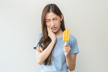 Face expression suffering from sensitive teeth and cold, asian young woman, girl hand touching her cheek, feeling hurt, pain eating ice cream, lolly. Toothache molar tooth at home, dental problem.