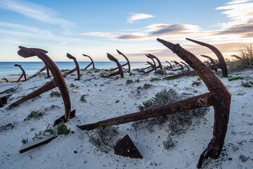 Rusty old anchors on the beach at the Anchor Cemetary graveyard at Praia do Barril beach in Tavira,...