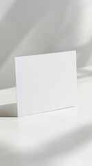 Title: Blank white card on a white surface with a soft shadow, providing a minimalist and modern setting ideal for showcasing branding, invitations, or product advertisements.

