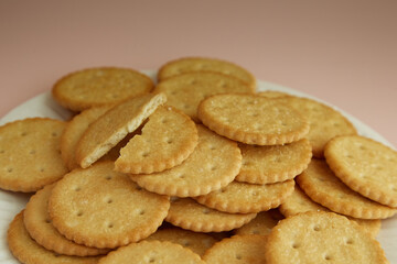 Crackers on a disposable plate and one cookie broken in half on a pink background, Salty crackers on a pink background close-up