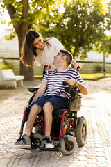 A young woman cares for her disabled brother in an automatic wheelchair at an outdoor park....