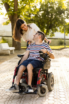 A young woman cares for her disabled brother in an automatic wheelchair at an outdoor park. Disabled woman and man look at each other happily.Concept of men with cerebral palsy.