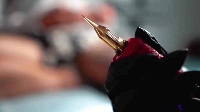 A tattoo artist in a tattoo parlor draws a design with black paint on the client&rsquo;s skin. Machine needle close-up. Art and beauty on the male and female body