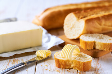 Cut slice baguettes with butter on a light kitchen table.