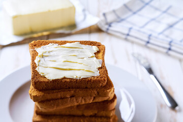 Stack of slices of toast bread slices with butter, on a white table.