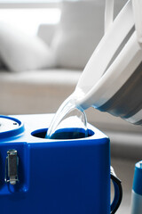 Pouring detergent into extractor. Keep couch tidy using cleaning equipment. Household chores....