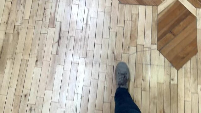 Feet in grey sneakers walking and stepping over parquet floor