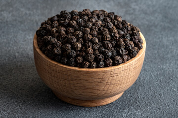 Black peppercorns in wooden bowl on gray dark concrete background
