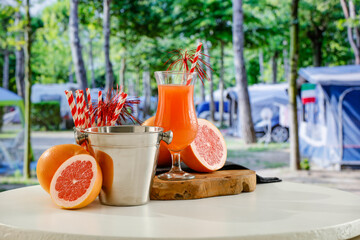 Fruit juice in glass on wooden board table top with blurred campsite background
